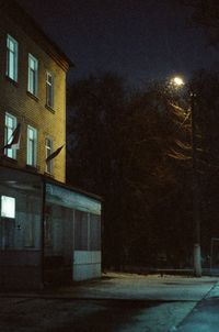 Illuminated street by building against sky at night