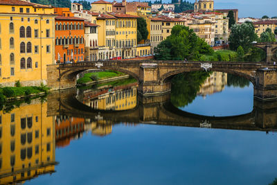 Arch bridge over river by buildings against sky in city