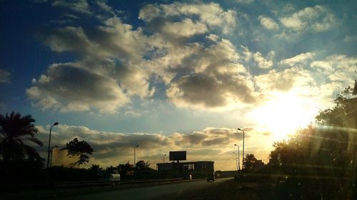 Cars on road against cloudy sky on sunny day