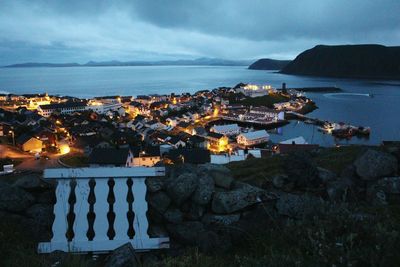 Illuminated city by sea against sky