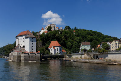 Buildings by river against blue sky