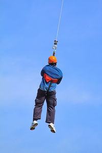 Low angle view of man holding rope against clear blue sky