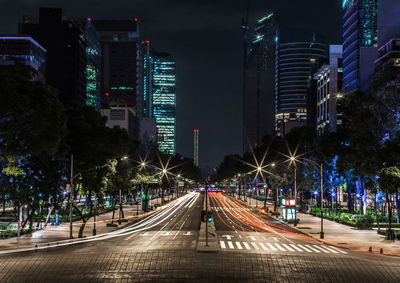 Light trails over illuminated street amidst buildings in city at night