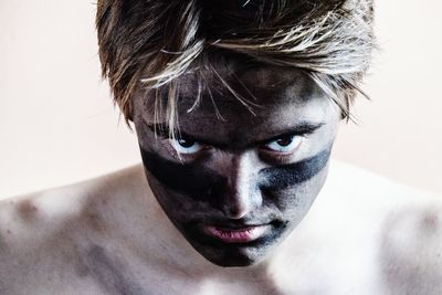 Close-up portrait of serious shirtless man with face paint against white background