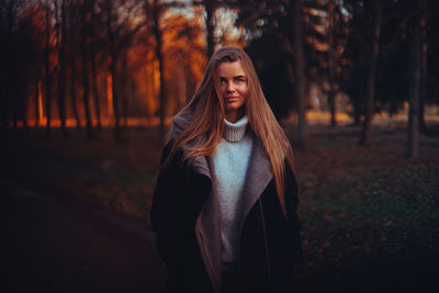 Portrait of young woman standing in forest during sunset