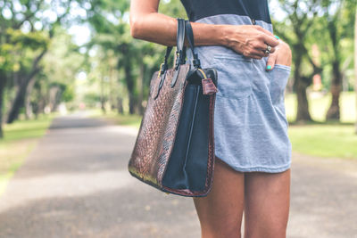 A girl walks in the park, in her hands a bag made of python skin