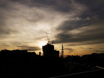 Silhouette of factory against sky during sunset