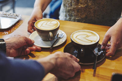 Midsection of man holding coffee cup on table