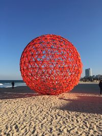 Red ball on beach against clear blue sky