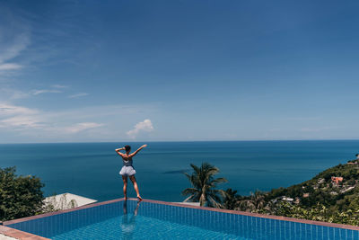 Woman standing by swimming pool against sea