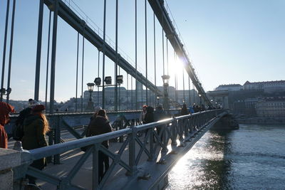 People on bridge in city against sky