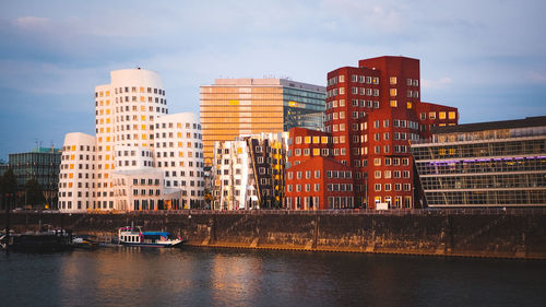 Buildings by river against sky in city