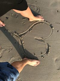 Low section of couple standing by heart shape on beach