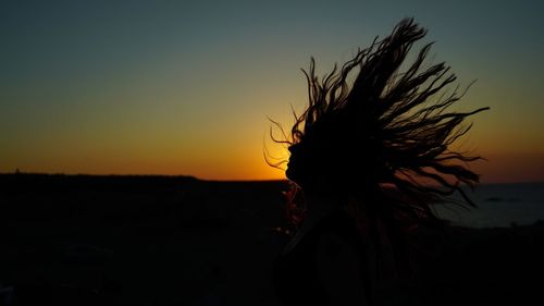 Silhouette woman tossing hair against clear sky during sunset