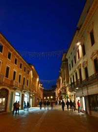 People on street amidst buildings in city at night