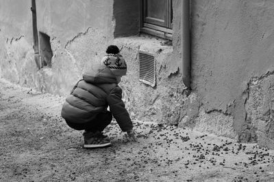 Rear view of boy crouching on footpath