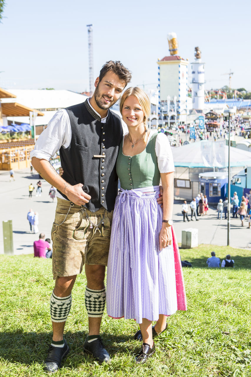 PORTRAIT OF SMILING YOUNG COUPLE STANDING AGAINST BUILDING