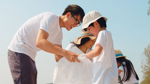 Parents with children collecting garbage standing against clear sky