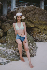 Full length of smiling woman sitting on rock at beach