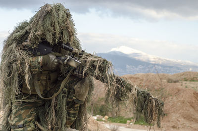 Sniper holding rifle against sky