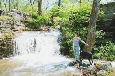 Woman with dog standing near waterfall in forest