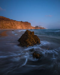 Rock formation on beach against sky during sunset