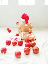 Rear view of child wearing santa hat while sitting by cake and ornaments on fabric during christmas