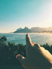 Cropped image of man pointing at mountain by sea against sky