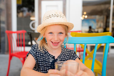 Portrait of cute girl wearing hat sitting at outdoor restaurant