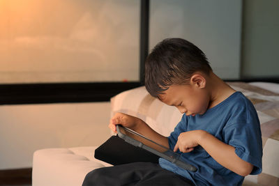 Boy using digital tablet while sitting on bed at home