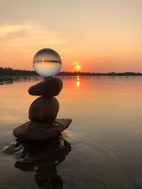 Stack of pebbles on lake against sky during sunset