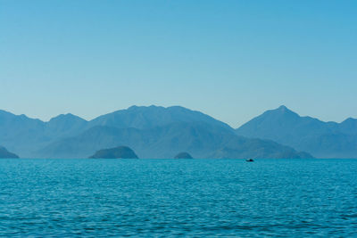 Scenic view of sea and mountains against clear blue sky