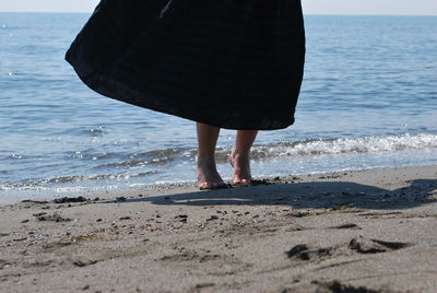 Low section of woman with surfboard walking at beach