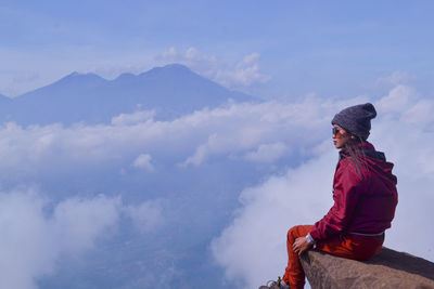 Man sitting on mountain against sky