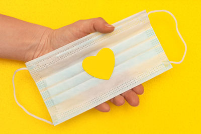 Close-up of hand holding heart shape against yellow background