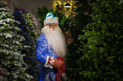 Portrait of santa clause standing amidst christmas trees