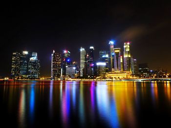 Illuminated buildings by river against sky at night