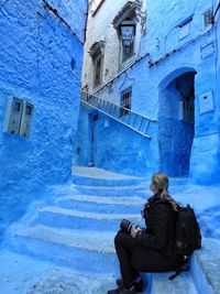 Woman holding camera looking away while sitting by built structure