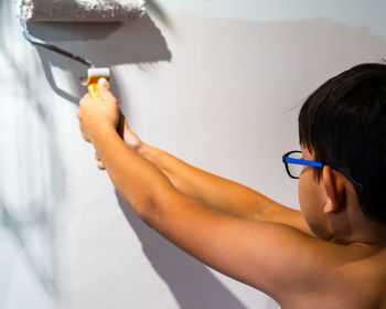 Repair in the apartment. happy child shirtless asian boy paints the wall with pastel pink paint.