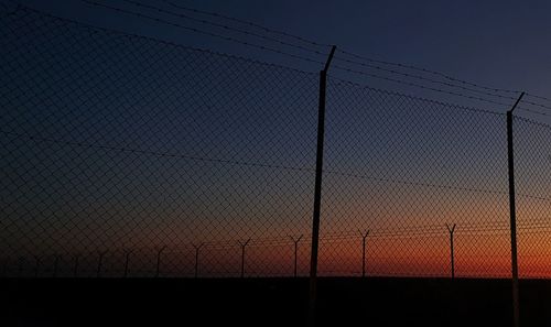 Silhouette chainlink fence against sky during sunset