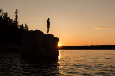 Silhouette woman standing on rock against sky during sunset