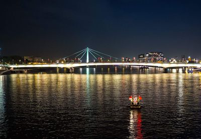 Illuminated bridge over river against sky in city at night