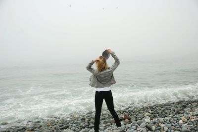 Full length of young woman standing at beach against clear sky