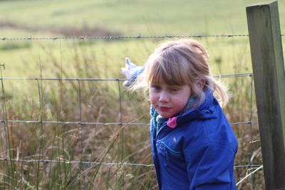 Portrait of girl winking while standing by fence