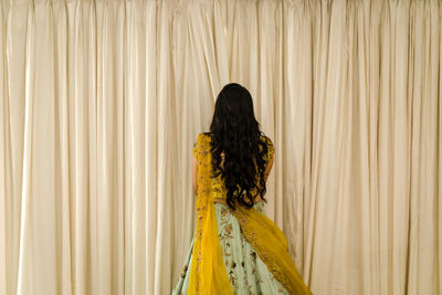 Rear view of woman standing against yellow background