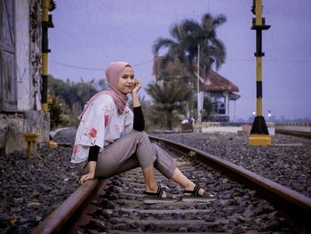 Full length of woman sitting on railroad track against sky