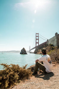 People sitting on bridge over sea against sky