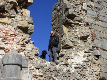 Low angle view of man and dog standing amidst damaged wall