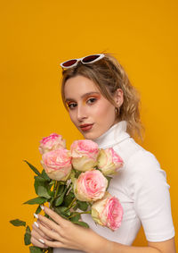 Portrait of woman holding rose bouquet against yellow background