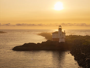 Lighthouse by sea against sky during sunset